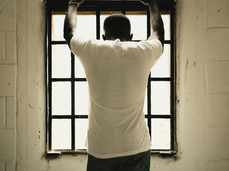 A man back turned with his hands up facing a window